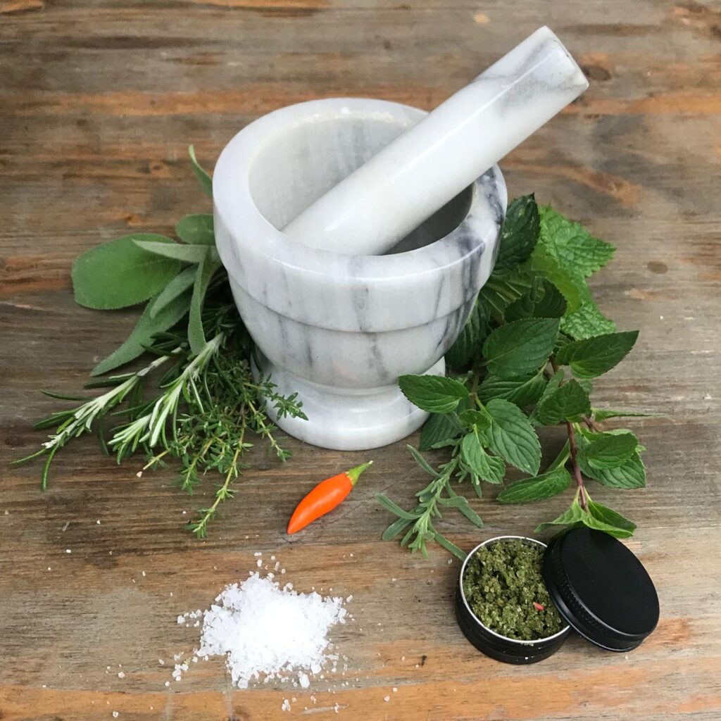 Tutto l'occorrente per realizzare il sale aromatico agli Orti Dipinti: sale, erbe aromatiche, mortaio e un barattolino del prodotto finito.